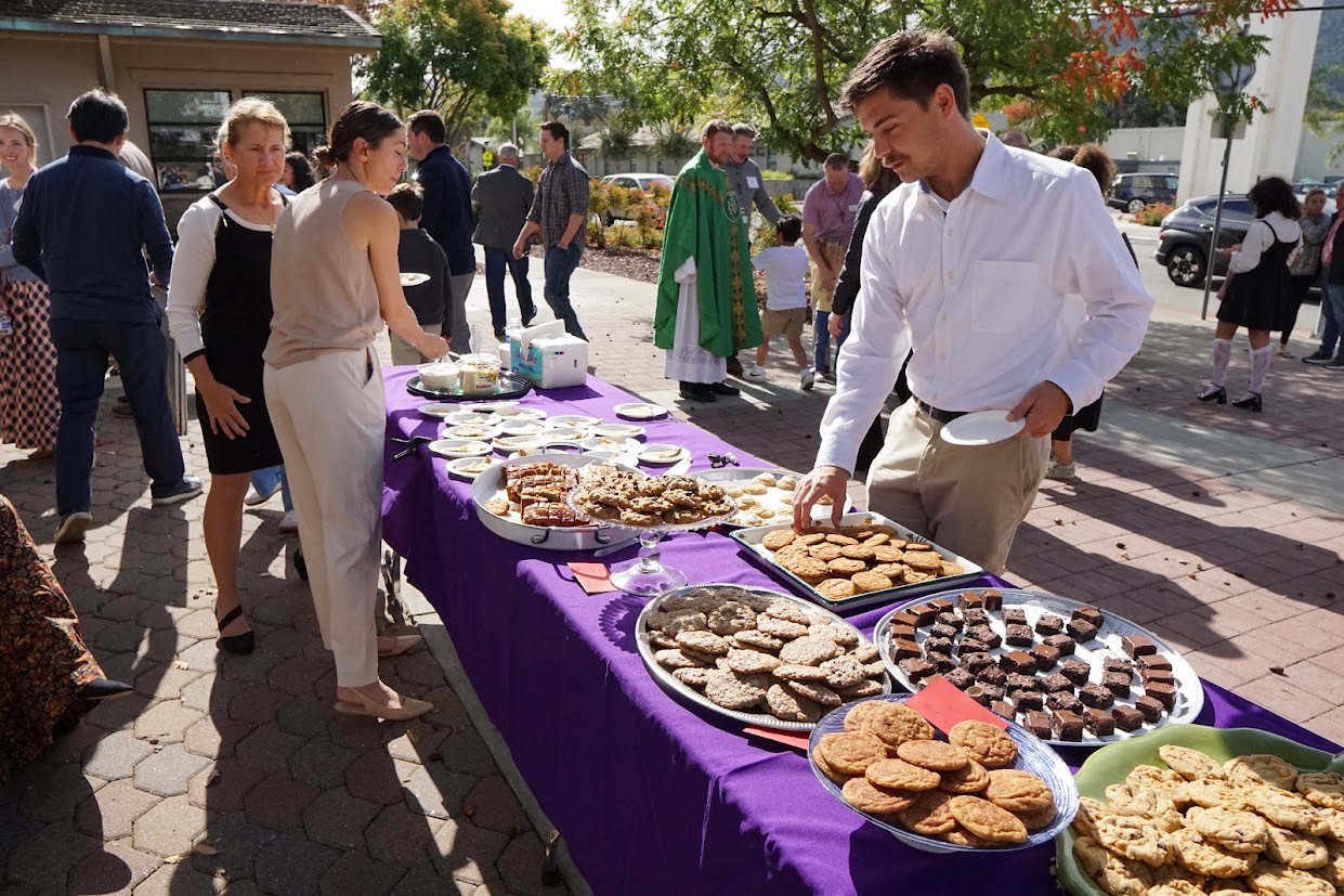 Parishioners gathering around a table of cookies and brownies outside the church after Mass
